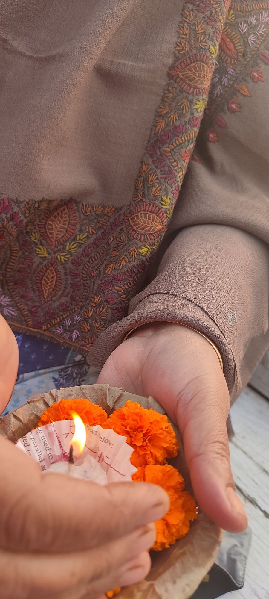 Hands holding a lit diya in a bed of marigolds
